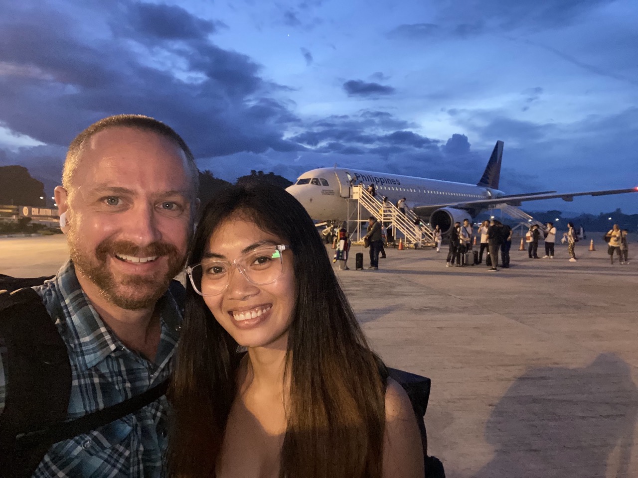 Rose and BC smiling on an airport tarmac in front of a plane
